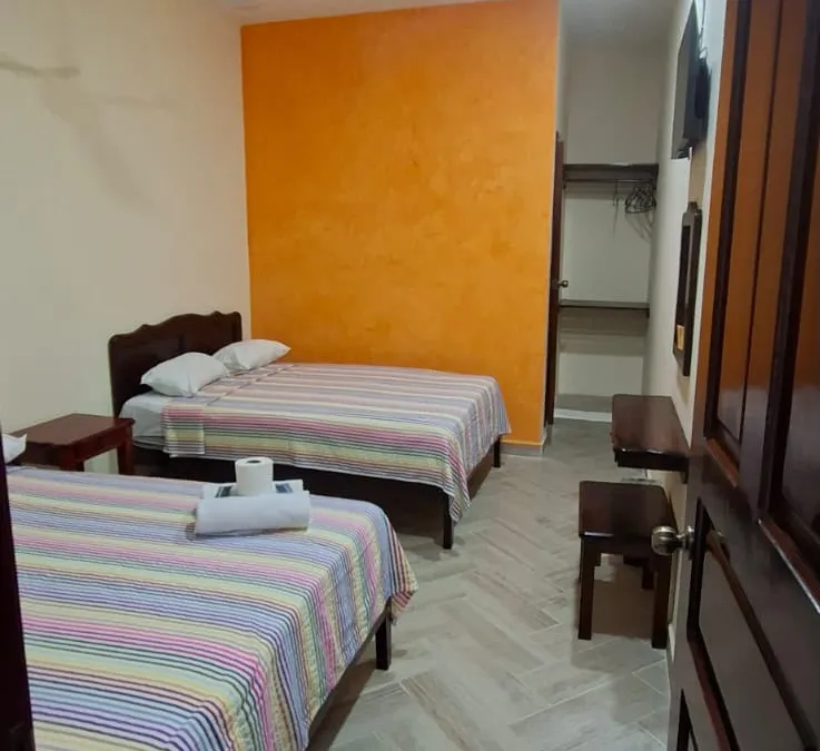 Habitación de Casa Llanos en Tecolutla con pared naranja, ventilador de techo y televisión