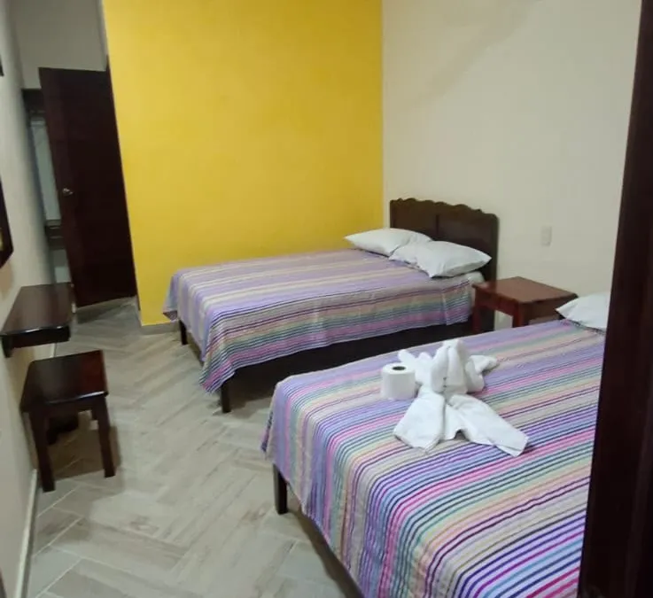 Habitación de Casa Llanos en Tecolutla con pared amarilla y dos camas matrimoniales